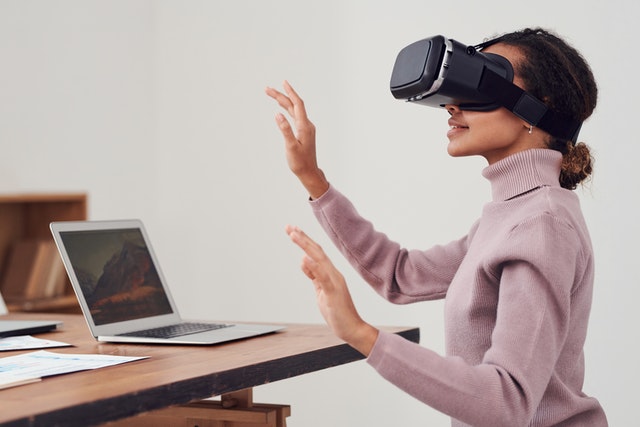 smiling woman with virtual reality eye wear on sitting in front of a laptop with her hands in the air in front of her